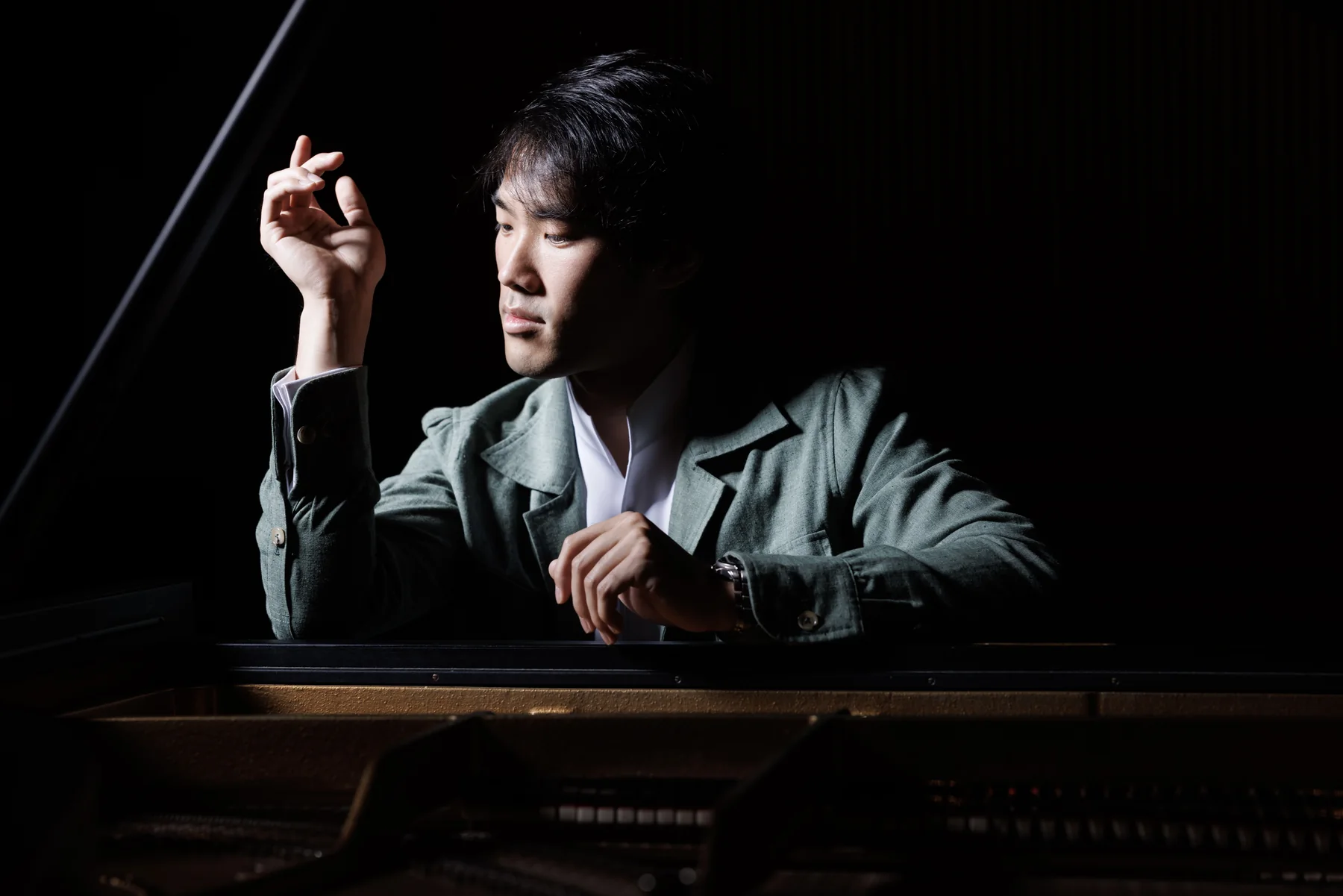 Bruce Liu leaning over a grand piano in a green jacket