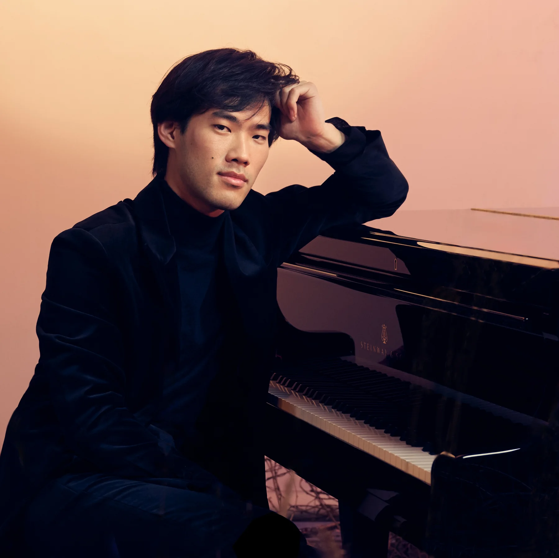 Bruce Liu seated beside a grand piano against an orange backdrop