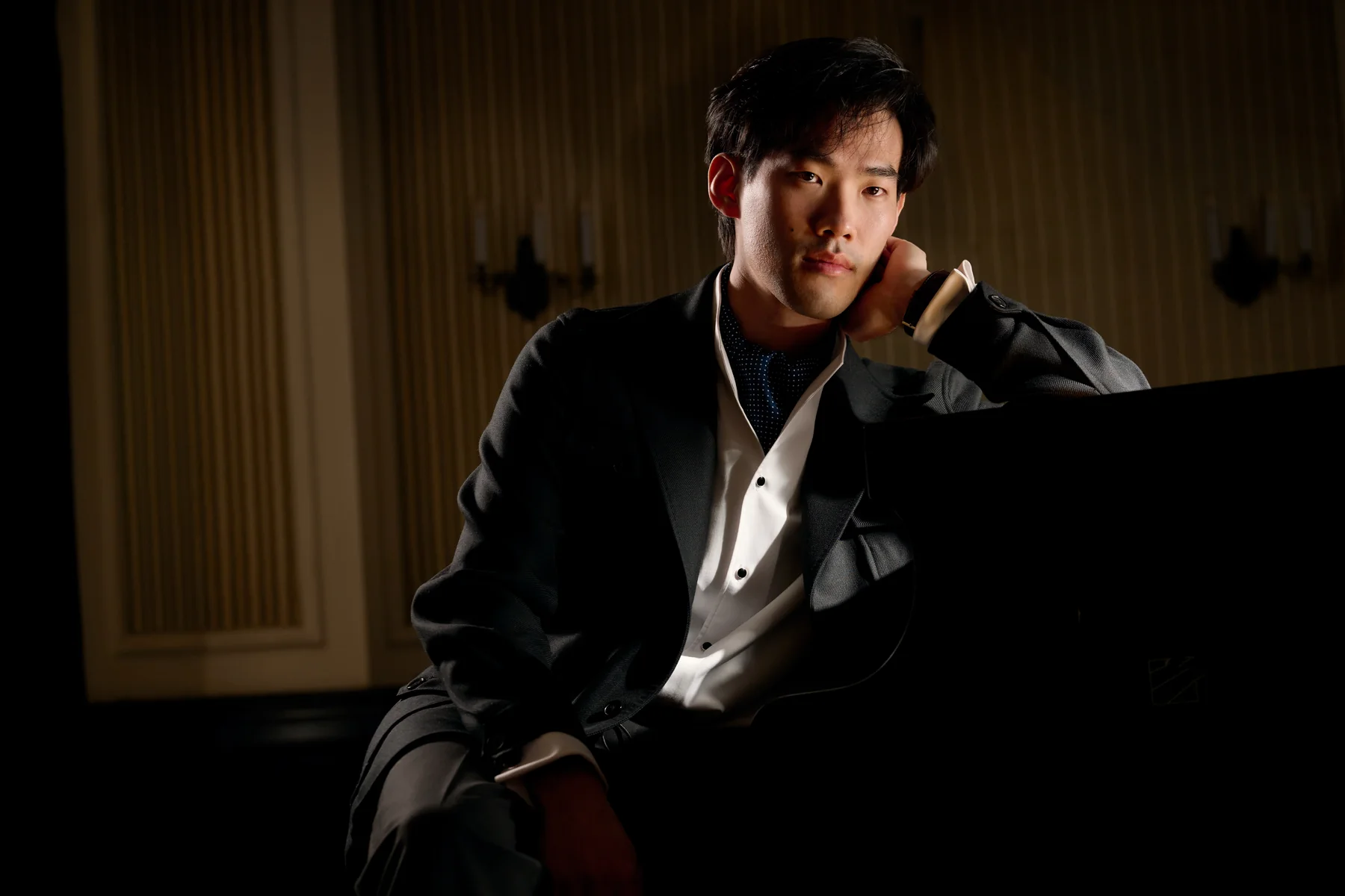 Bruce Liu seated beside a grand piano in a wood-panelled room