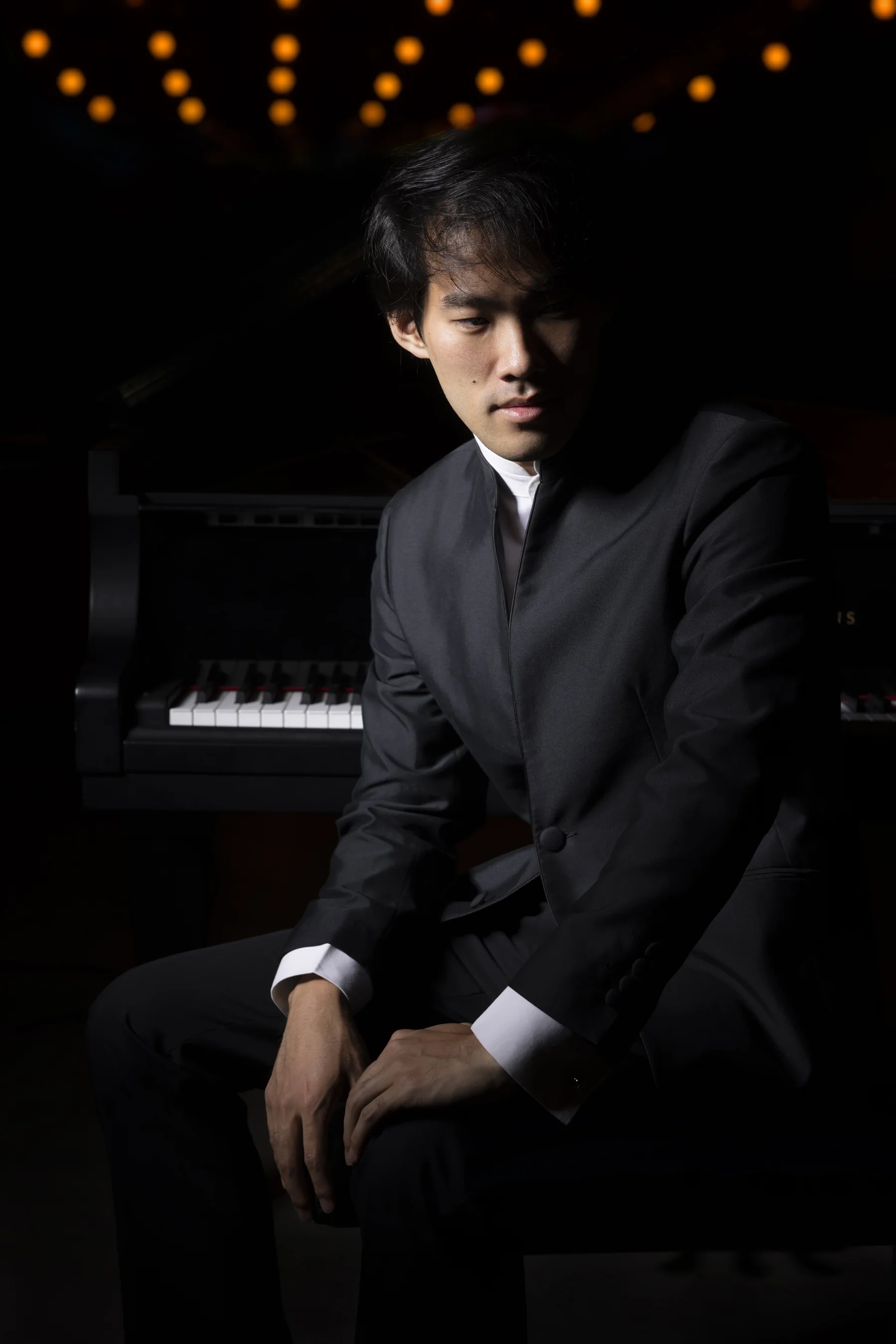 Bruce Liu seated at a piano beneath warm theatre lights